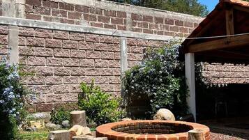 Un hogar de ladrillo rodeado de troncos de madera, frente a un muro de ladrillo bajo un cielo despejado.