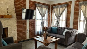 A living room with a brick wall, a flat-screen TV, a sofa set, a coffee table, and a fireplace. - Cabañas JH (Huasca)