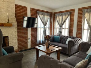 Un salón con pared de ladrillo, televisor de pantalla plana, conjunto de sofás, mesa de centro y chimenea.