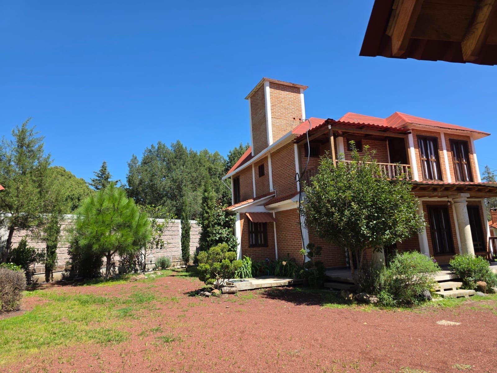 A two-story house with a red roof, a brick chimney, and a balcony.