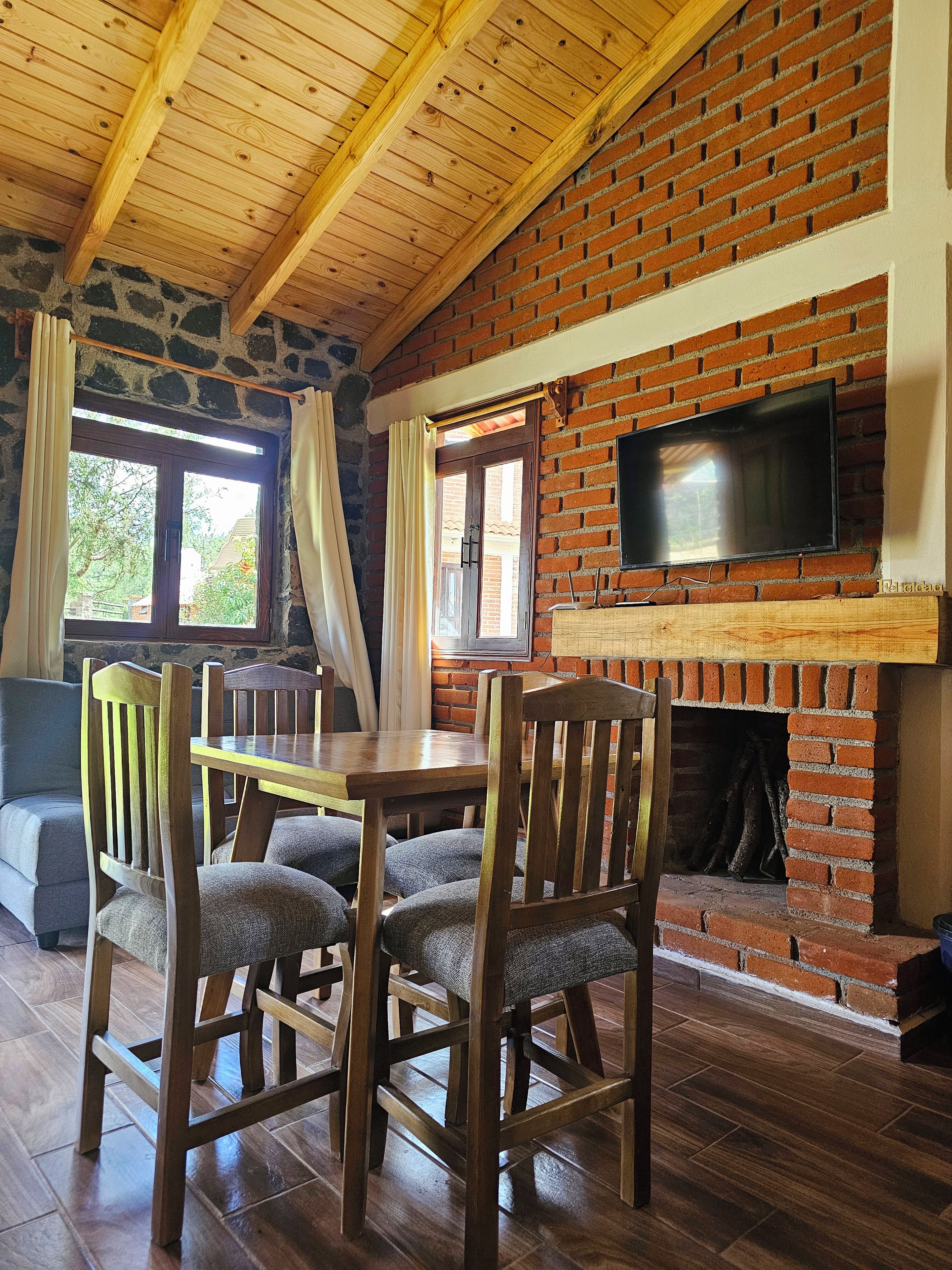 Zona pranzo con camino in mattoni, travi a vista in legno e televisore montato sopra.