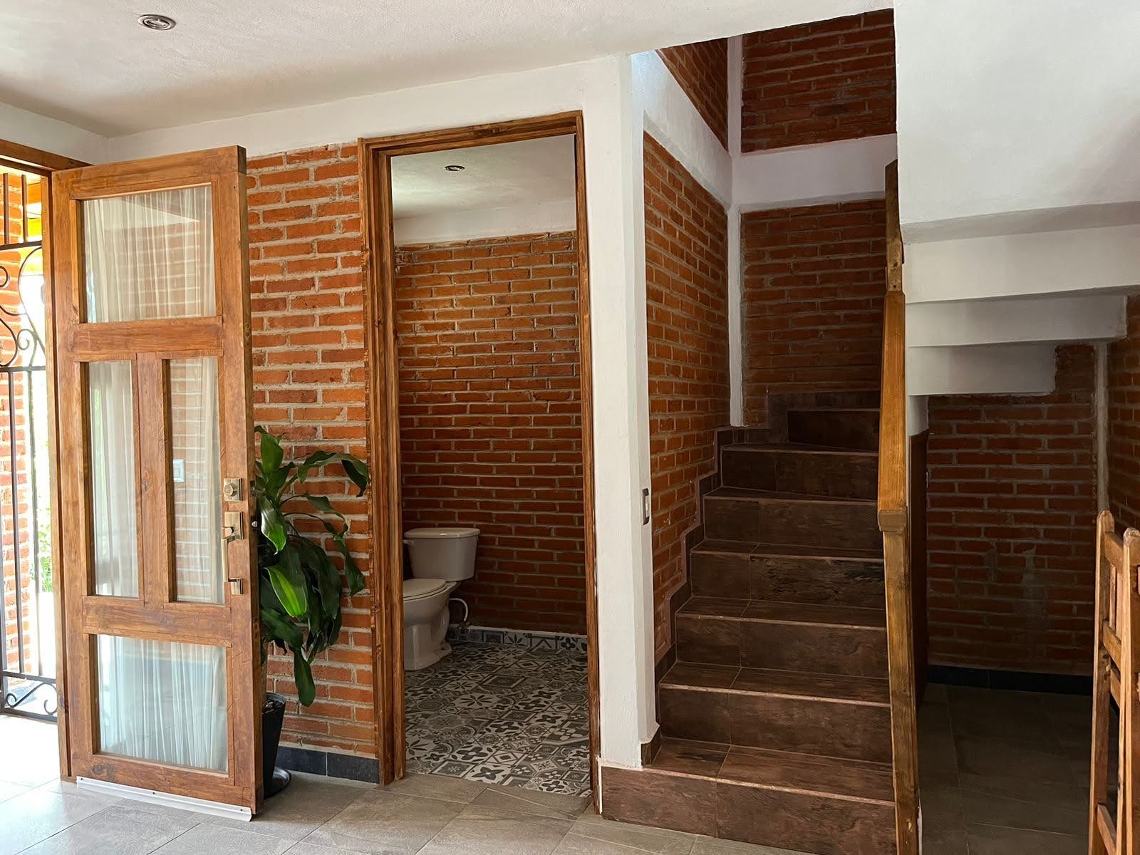 A staircase with wooden steps leading to a second floor, adjacent to a brick wall and a door with glass panels.