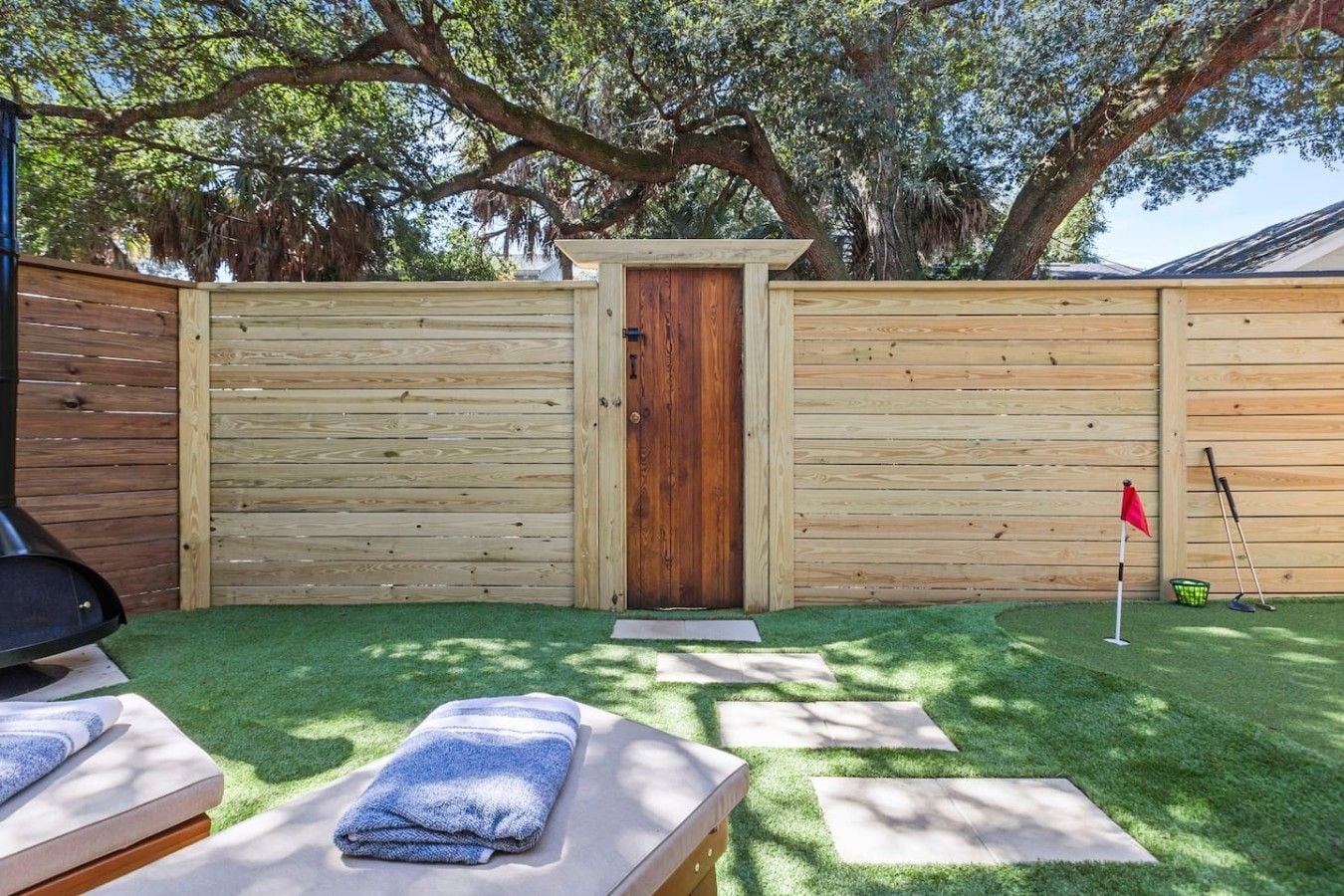 Une cour arrière avec une clôture en bois, une porte, un drapeau rouge et un club de golf.