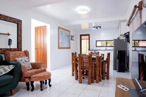 A modern living room with a green sofa, a wooden dining table, and a kitchen area with a refrigerator and stove.