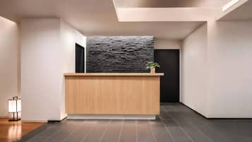 A reception desk with a modern design, a dark textured wall behind it, and a potted plant on top.