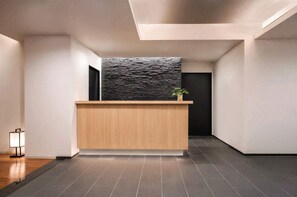 A reception desk with a modern design, a dark textured wall behind it, and a potted plant on top. - Oaks Vacation Club Kyoto Gojo (Kyoto)