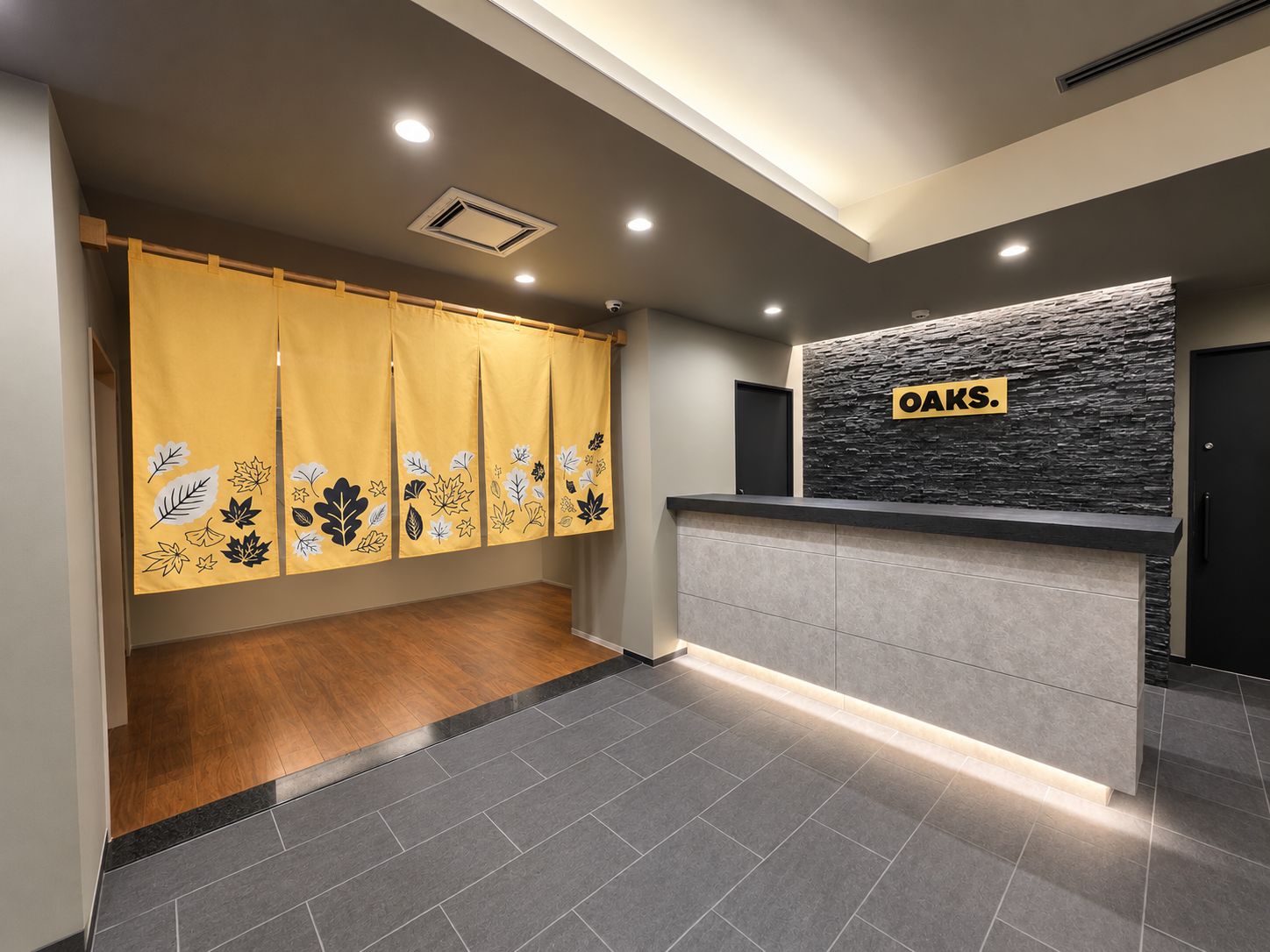 Zona de recepción con pared de textura de piedra, un mostrador de recepción y piso de madera.