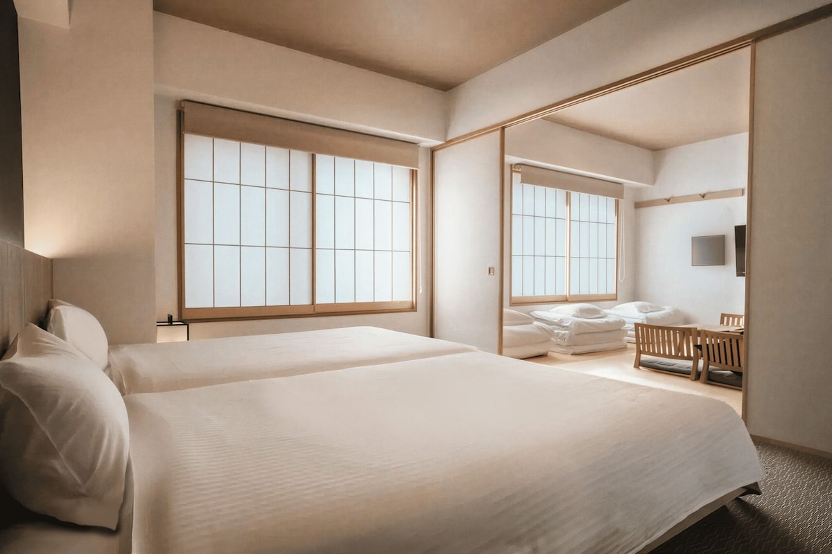 A hotel room with a large bed, a sitting area with a table and chairs, and a large window with a view.