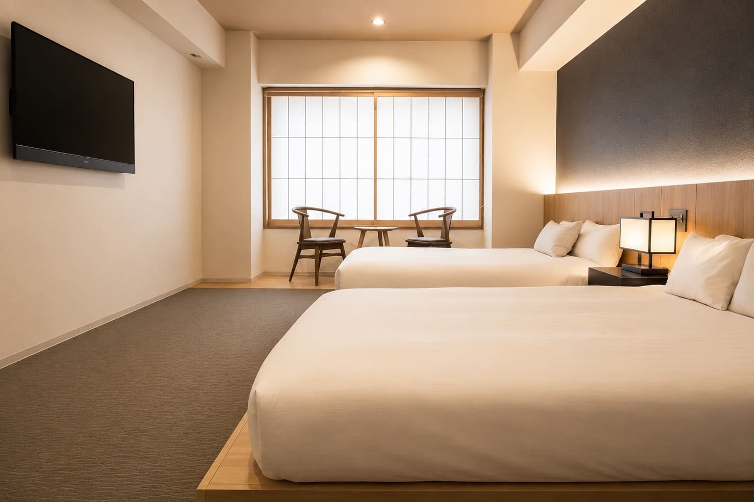 Habitación de hotel con dos camas, un televisor montado en la pared, una ventana con vistas y una pequeña mesa con sillas.