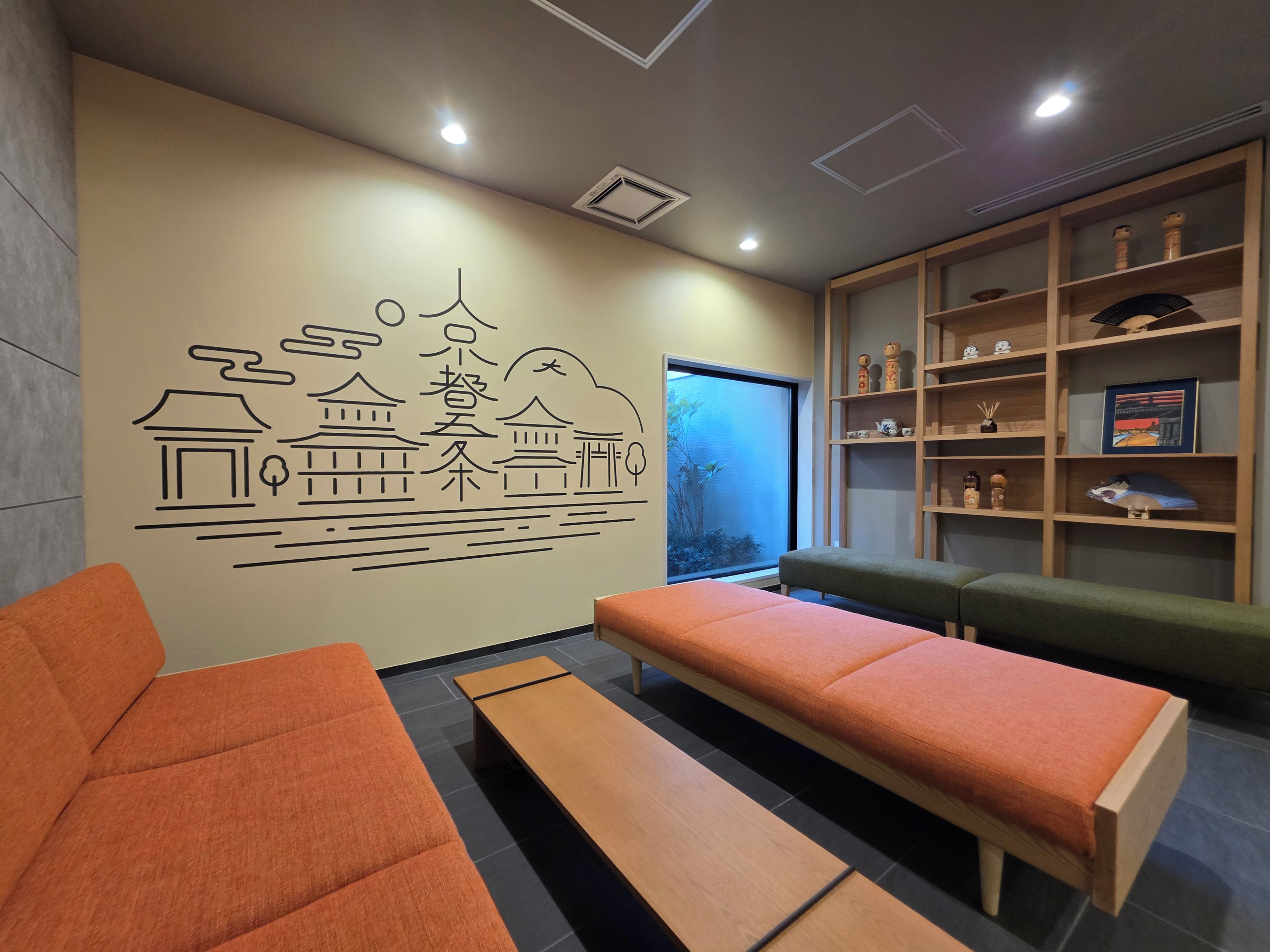A room with a wall mural depicting traditional architecture, a seating area with benches, and a shelf with decorative items.