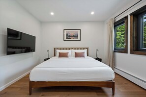 A bedroom with a wooden bed, white bedding, a mounted TV, and a window with curtains. - Twin Pines Lodge - Luxury Cabin, Kid Friendly (Catskill)