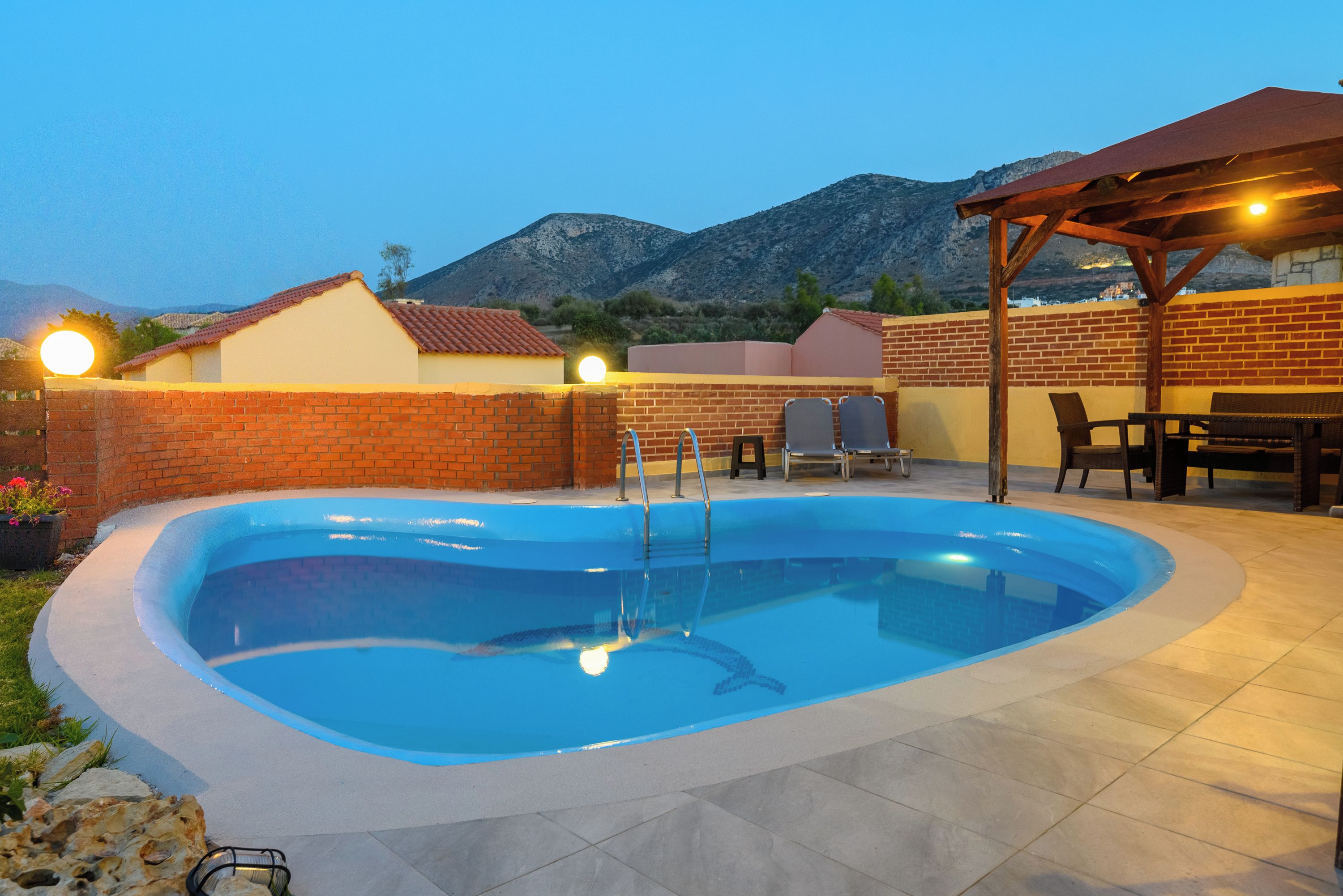 A swimming pool with a brick wall and a pergola with seating.