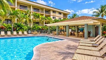 A hotel pool area with a clear blue pool, lounge chairs, and a covered seating area.