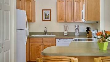 A kitchen with wooden cabinets, a refrigerator, a dishwasher, a coffee maker, and a blender.