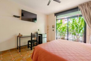 A bedroom with a bed, a desk, a chair, a television on the wall, and a view of greenery outside. - MEXHICCO33 (El Salto)