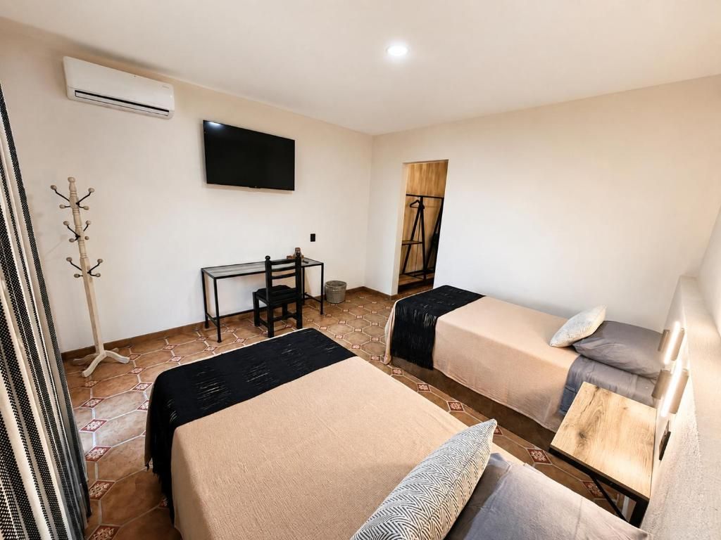 A hotel room with two beds, a desk, a chair, a TV, and a coat rack.