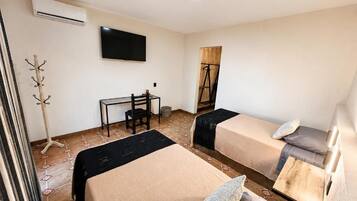 A hotel room with two beds, a desk, a chair, a TV, and a coat rack.