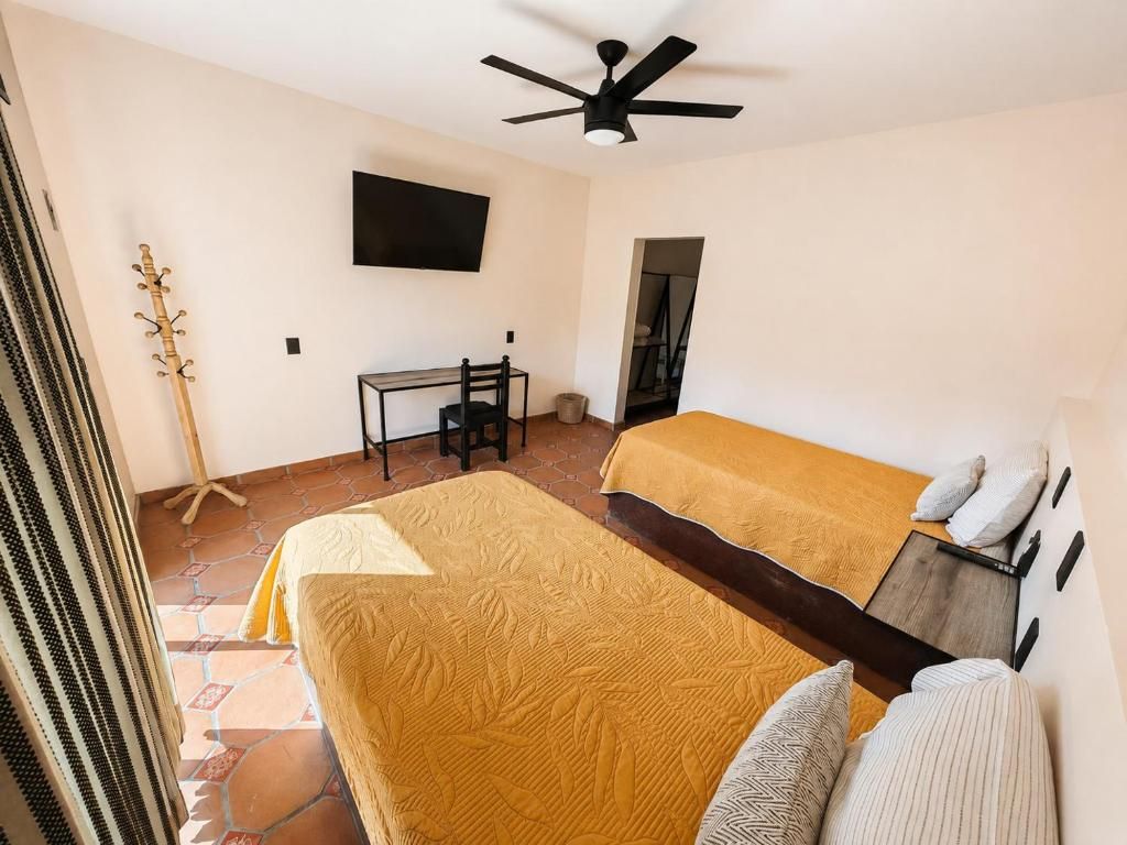 A room with two beds, a desk, a chair, a television, and a ceiling fan.