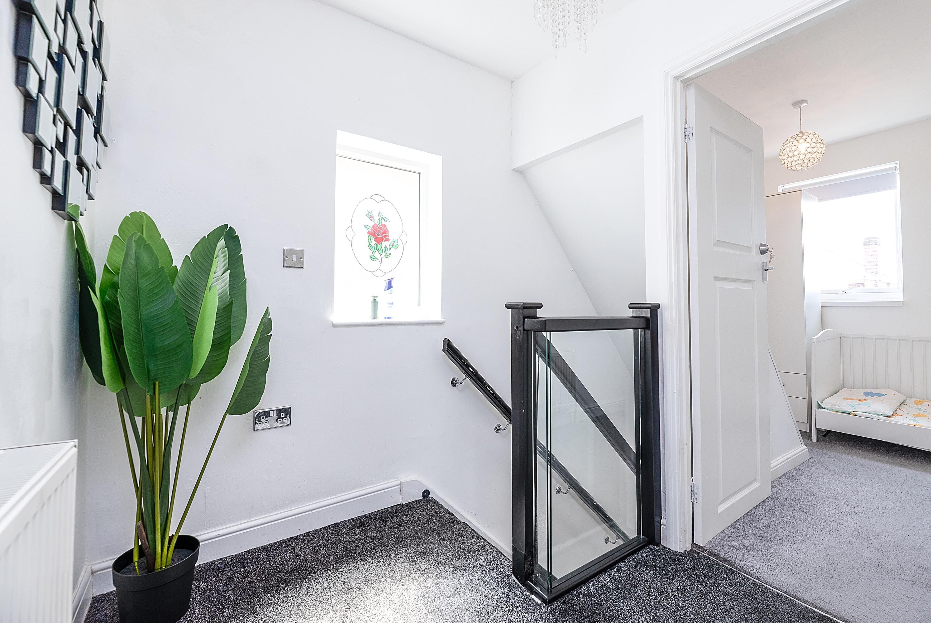 A hallway with a potted plant, a framed artwork, a door with a glass panel, and a staircase leading to another room.