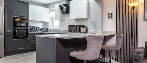 A modern kitchen with a central island, bar stools, and a built-in oven.