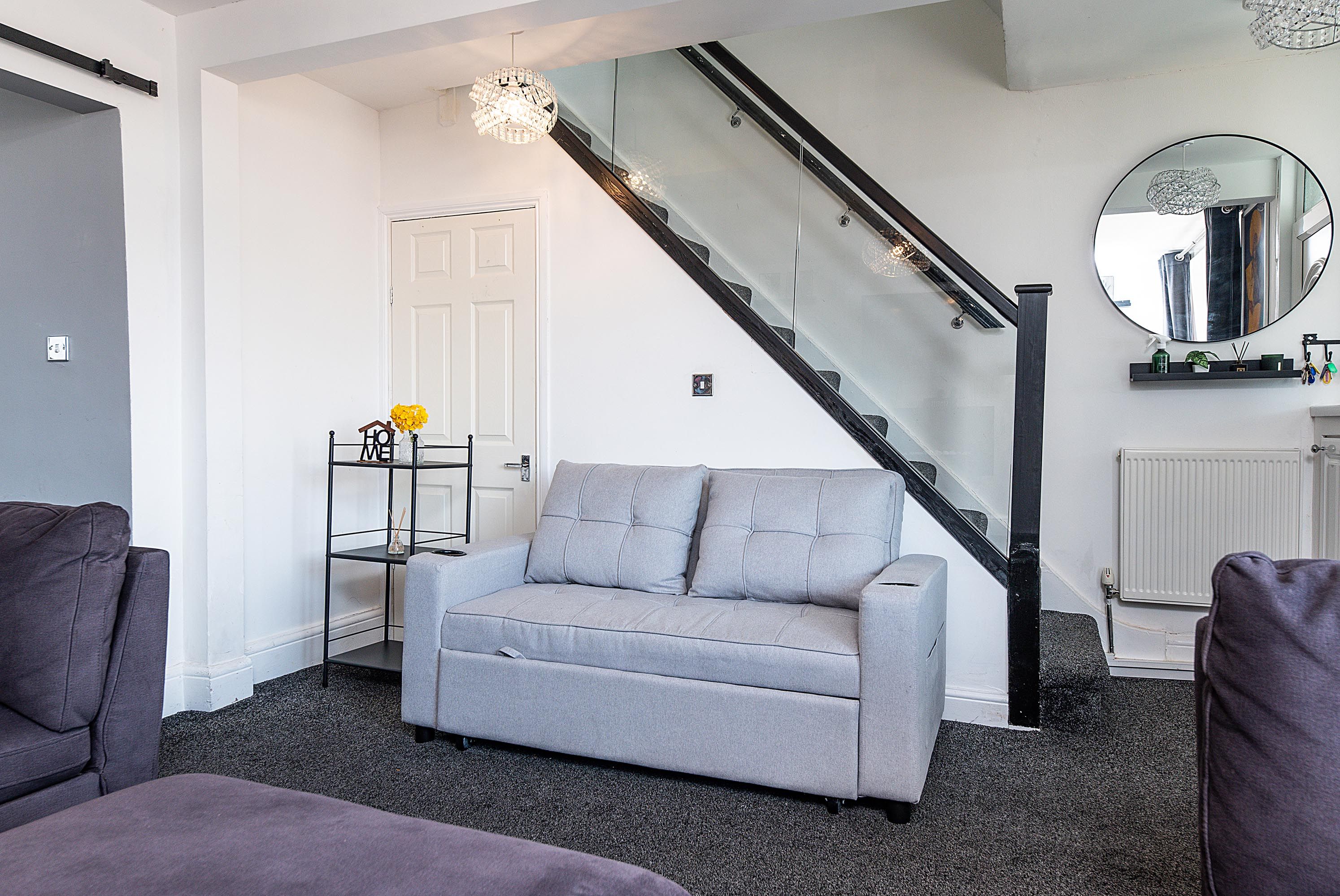 A modern living room with a grey sofa, a staircase, and a mirror on the wall.
