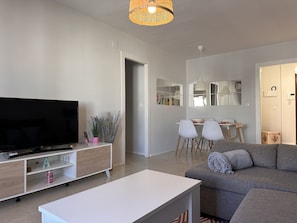 A modern living room with a flat-screen TV, a white coffee table, a grey sofa, and a dining area with chairs and a table. - Apartamento Texas Life - Ole Solutions (Jerez de la Frontera)