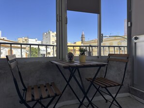 A balcony with a view of city buildings, a table, two chairs, and a potted plant. - Apartamento Texas Life - Ole Solutions (Jerez de la Frontera)