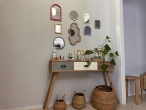 A room with a wooden console table, multiple wall mirrors, a clock, a potted plant, and woven baskets. - Apartamento Texas Life - Ole Solutions (Jerez de la Frontera)