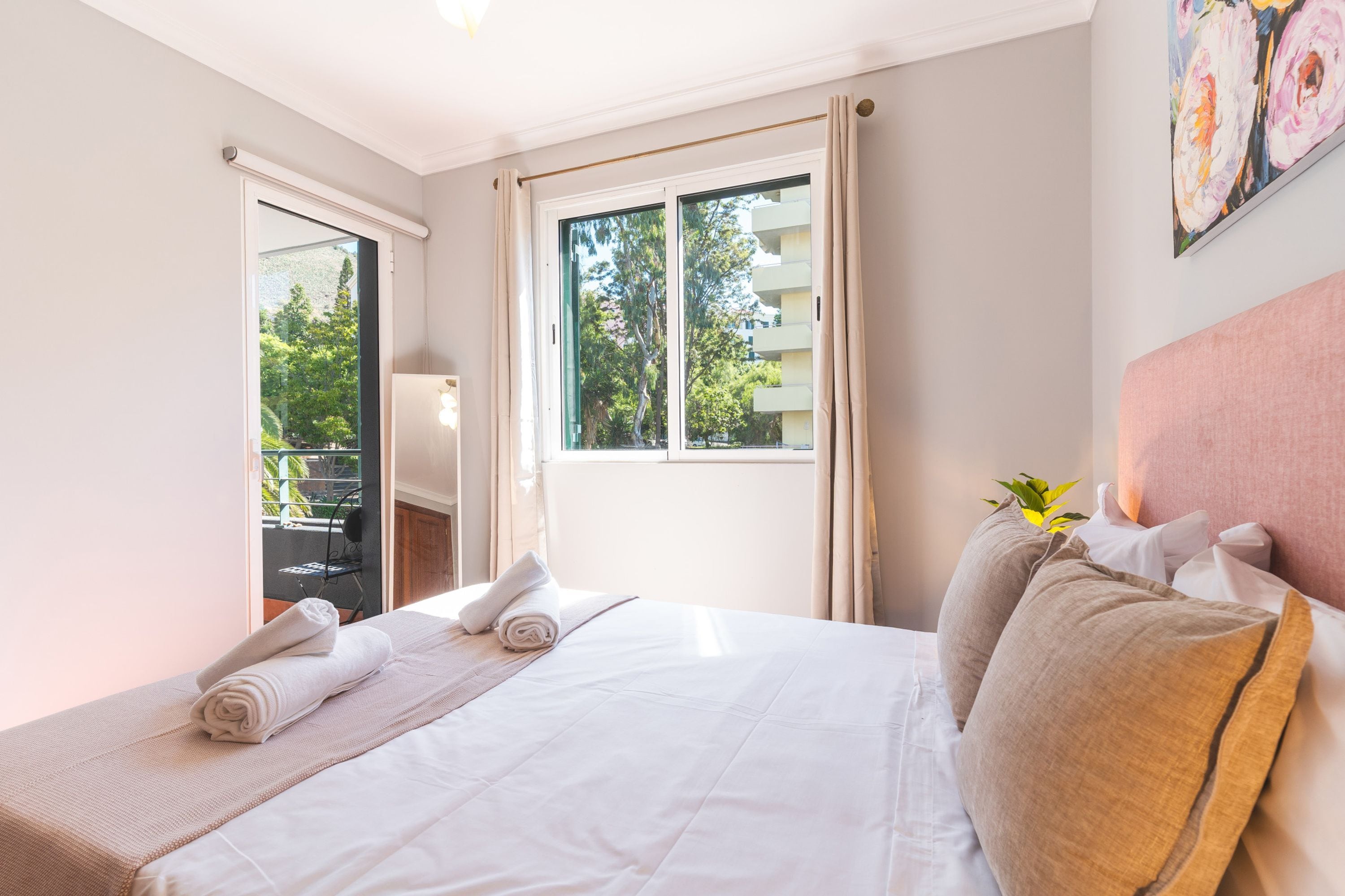 A hotel room with a bed, a window with curtains, a chair, and a plant.
