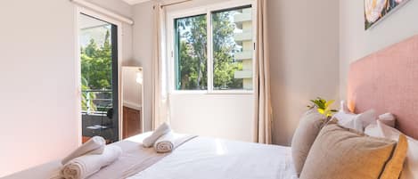 A hotel room with a bed, a window with curtains, a chair, and a plant.