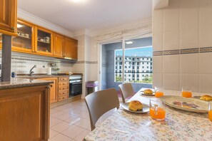 A kitchen with wooden cabinets, a dining table with chairs, and a view of buildings through the window. - Musa d Ajuda by Atlantic Holiday (Funchal)