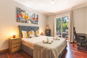 Hotellihuone, jossa on suuri sänky, työpöytä, tuoli, yöpöytä, lamppu ja taulu seinällä.