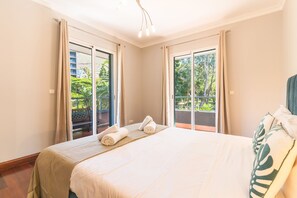 Ein Hotelzimmer mit einem großen Bett, zwei mit Vorhängen versehenen Fenstern, einer Sitzbank und Blick auf Grünflächen.