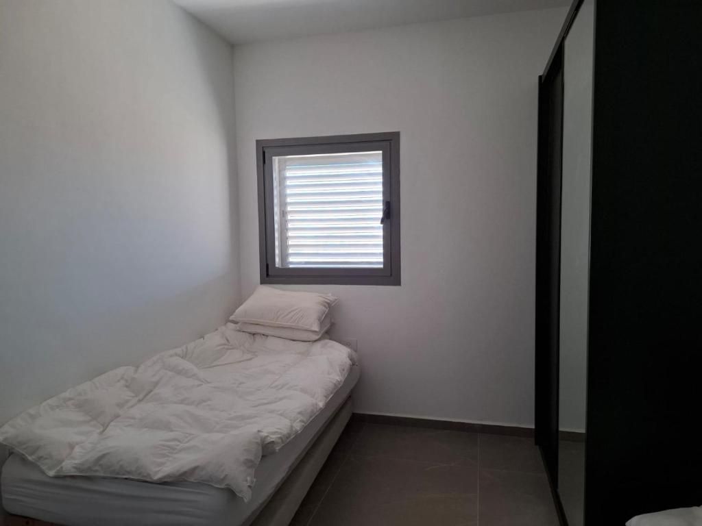 A small, single-bed room with a window, plain walls, and a tiled floor.