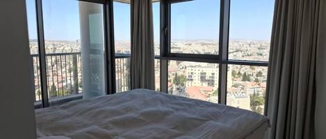 Une chambre avec un grand lit, deux fenêtres et une vue sur le paysage urbain.
