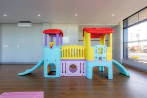 Una estructura de juegos infantiles en una habitación con suelo de madera, una ventana con vista a la calle y un equipo de aire acondicionado en la pared.