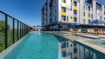 Un hotel moderno con piscina, mobiliario exterior y vistas a la ciudad.