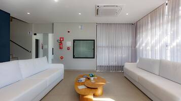 A modern living room with two white sofas, a wooden coffee table, and a glass door leading to a balcony.