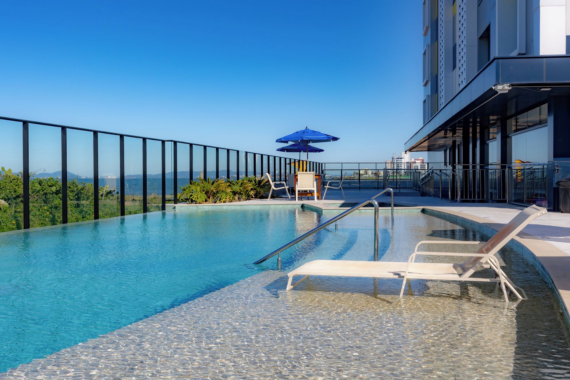 Una piscina infinita con agua cristalina, una sombrilla azul y sillones de descanso.