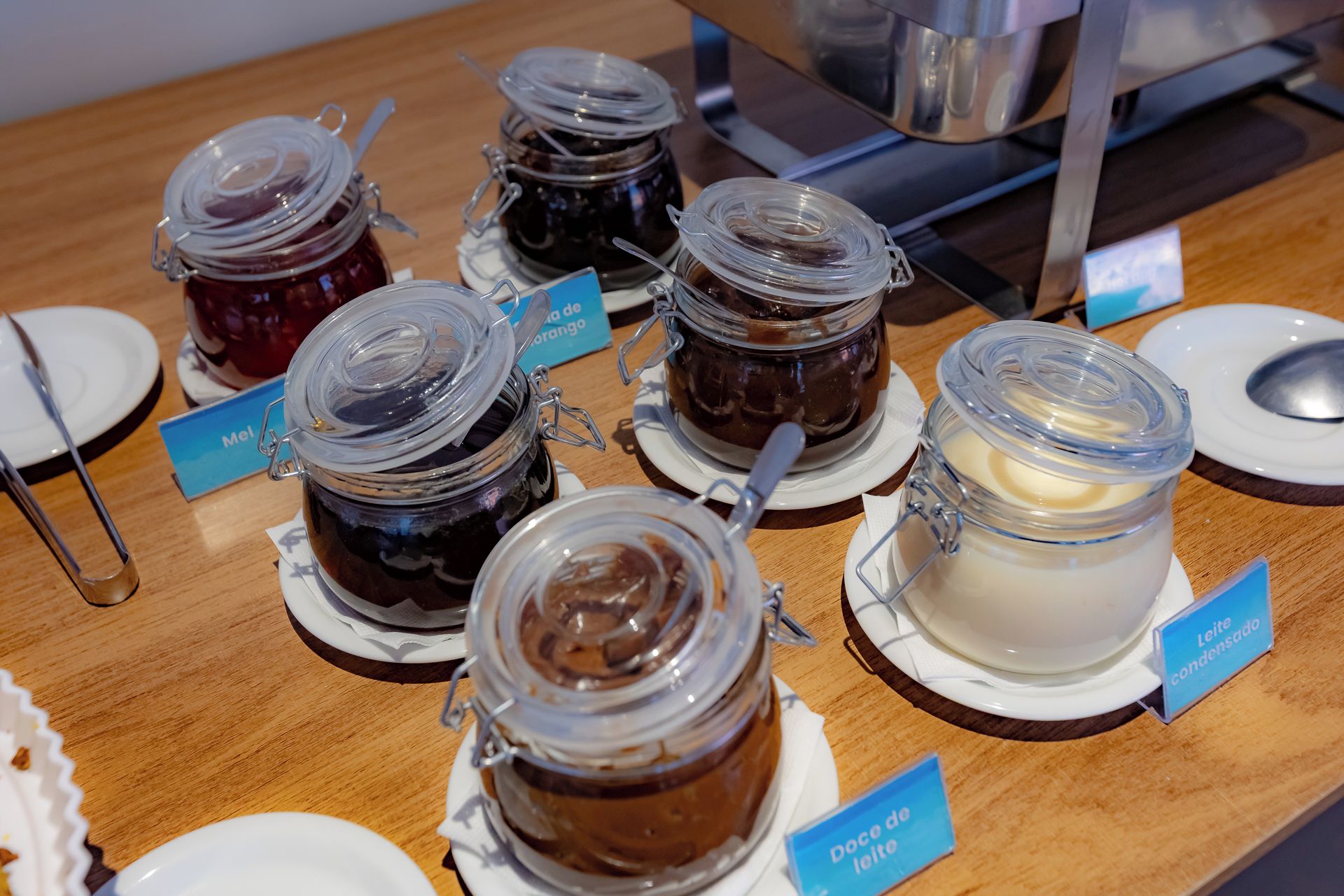 Una exhibición de diversos alimentos en frascos de vidrio con etiquetas, dispuestos sobre una mesa de madera.