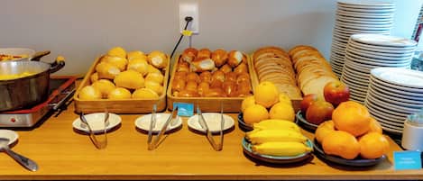A buffet with various food items including bread, pastries, fruits, and a pot of food on a stove.