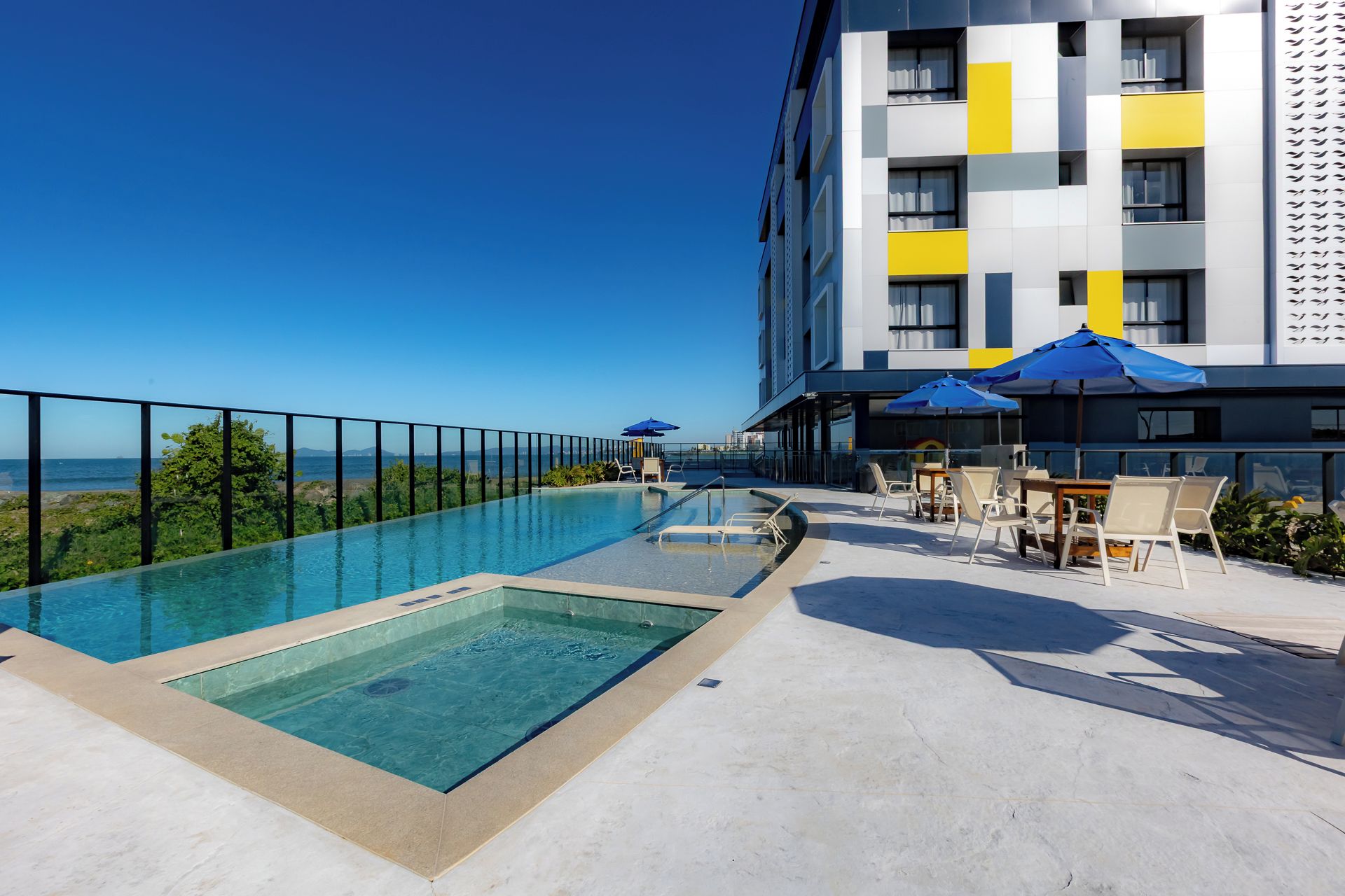 A rooftop pool with a clear view of the sea, surrounded by outdoor seating and umbrellas.