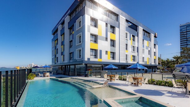 A modern hotel with a pool area, outdoor seating, and a view of the city skyline. - Bella Vista By Candeias (Barra Velha)