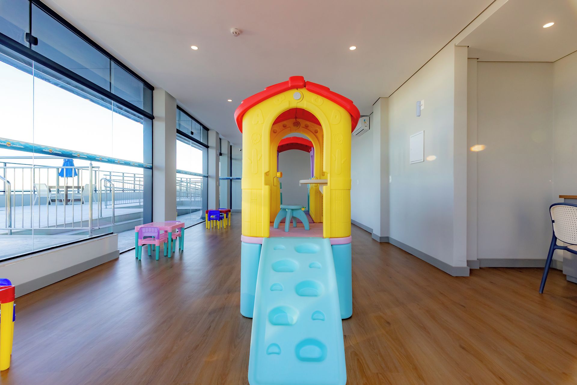 Zona de juegos infantiles con un tobogán y estructura de escalada, ubicada en una sala amplia con ventanas grandes y vistas al exterior.