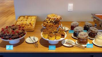 A buffet table with various desserts and spreads, including chocolate cake, lemon bars, and jams.