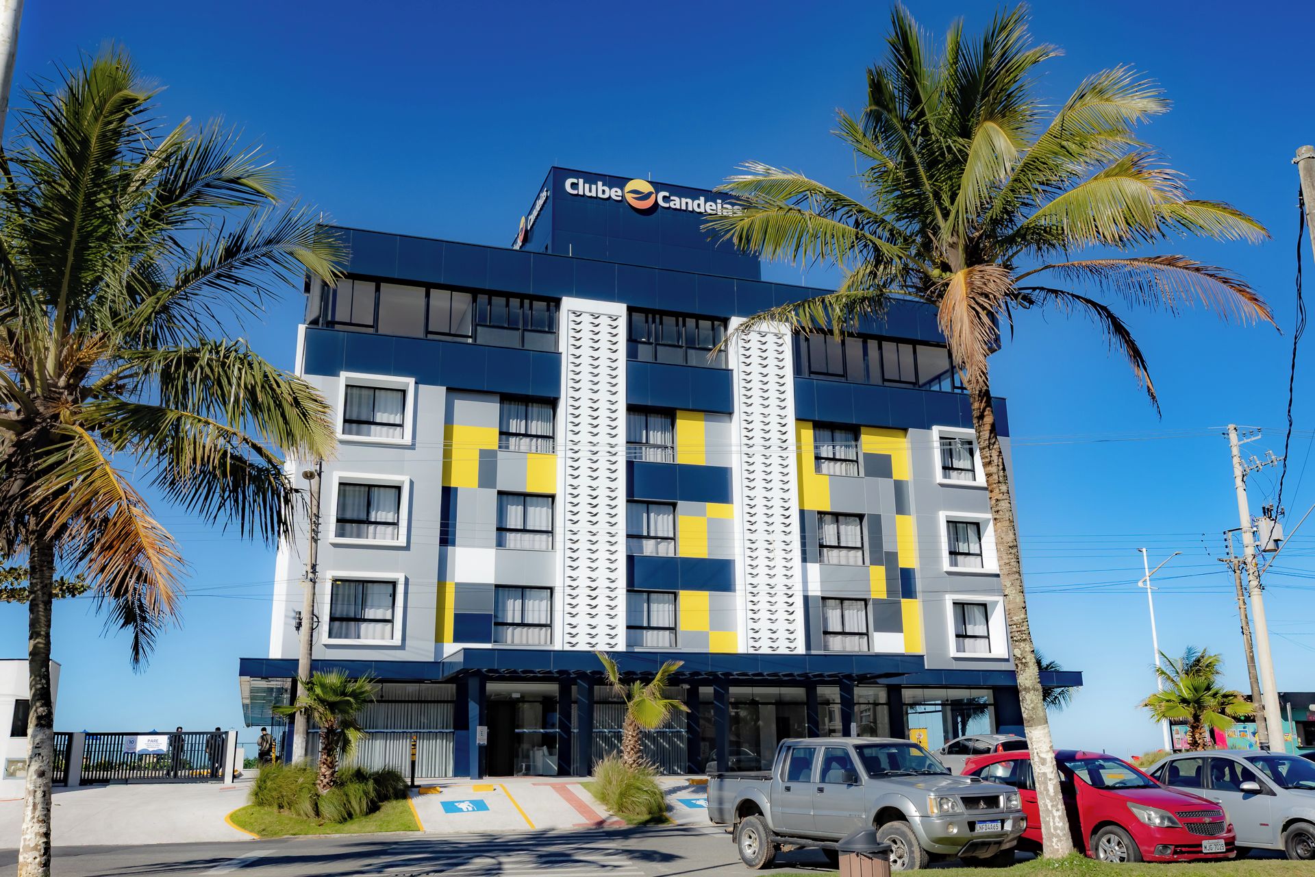Un hotel con fachada moderna, varios balcones y un estacionamiento con autos.