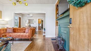 Un salon spacieux avec un canapé, une table basse et un tapis à motifs. Une porte en bois, ornée d’une guirlande verte, se trouve sur la droite.