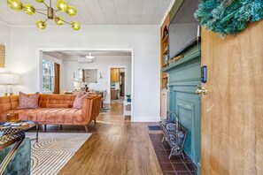 Een ruime woonkamer met een bank, een salontafel en een kamerkleed. Een houten deur met een groene krans bevindt zich rechts.