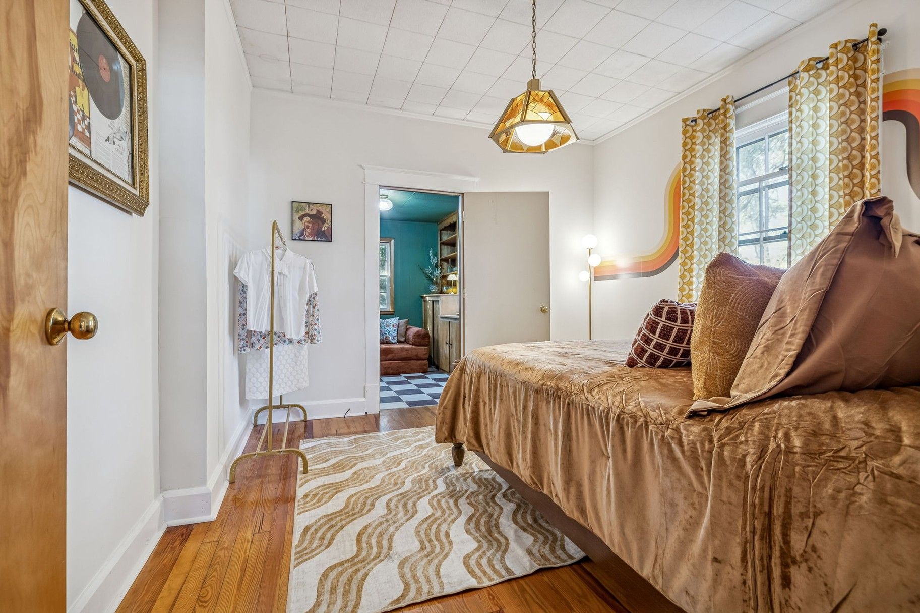 A bedroom with a bed, a hanging light fixture, a patterned rug, and a door with a brass handle.