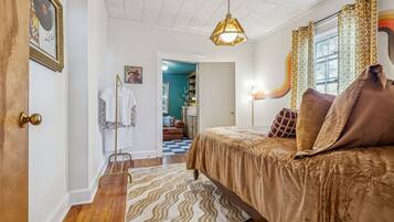 A bedroom with a bed, a hanging light fixture, a patterned rug, and a door with a brass handle.